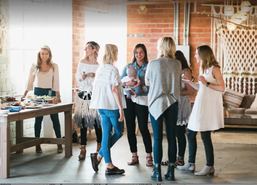 Guests mingling beside the catering table under the macramé wall hanging at Brick + Laurel