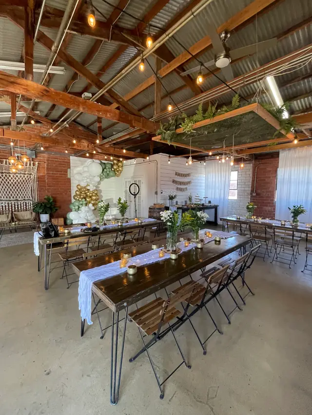 The empty Brick + Laurel room set for a dinner with long dark-wood tables, white runners and string lights