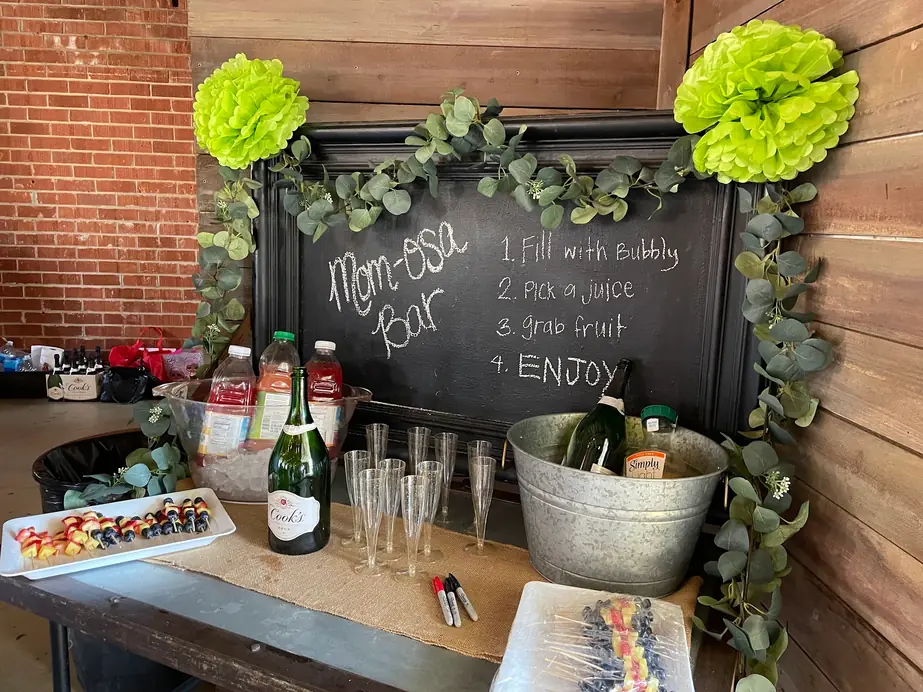 A mom-osa bar set up under the Brick + Laurel chalkboard with bubbly and juice